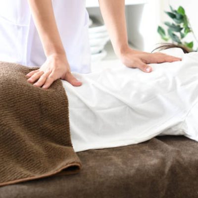 A young Asian woman lying face down receiving massage (manipulative) treatment in bed